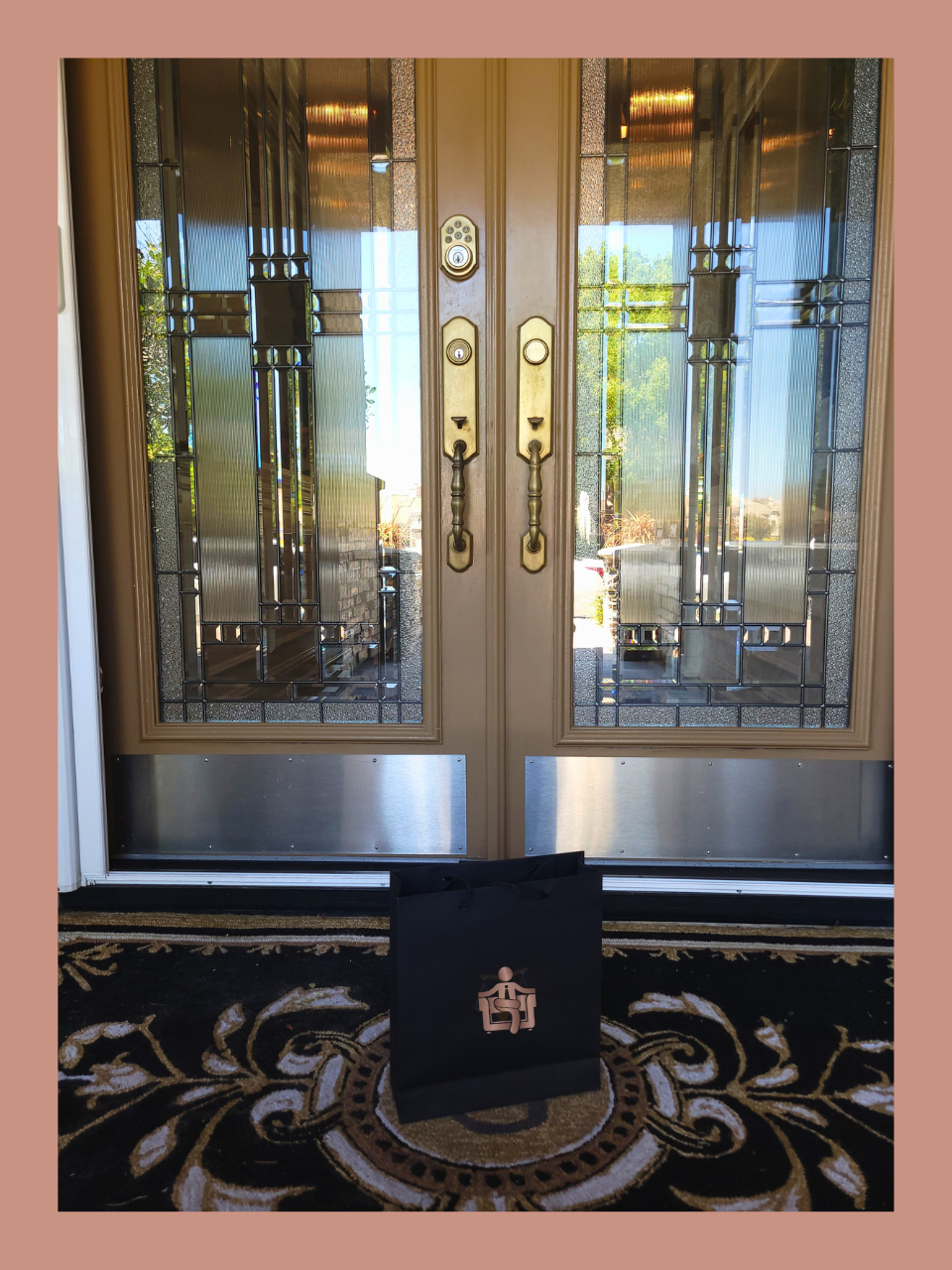 Black briefcase with a gold emblem on a decorative rug in front of glass doors.